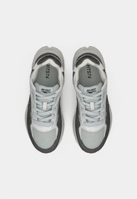 Chaussures de sport grises et blanches avec des panneaux en mesh et des accents noirs contrastants, dotées d'un système de laçage et d'une semelle en caoutchouc texturée.
