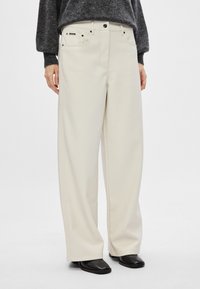 Φαρδιά, κρεμ χρώματος παντελόνια από μαλακό ύφασμα, με κλασικό σχέδιο πέντε τσεπών και μαύρο κούμπω.