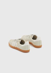 Vita lädersneakers med en texturerad yta, som har tre vita ränder, en sula i gummimaterial och en stoppad häl för stöd.