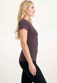 Violetti istuva t-paita lyhyillä hihoilla, sileä rakenne ja pyöreä kaula-auko. Yhdistetty mustiin legginsseihin, esitelty sivuprofiilista.