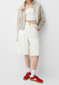 Light beige cropped jacket, white strapless top, high-waisted white denim shorts, and red sneakers with white accents. Plain background.