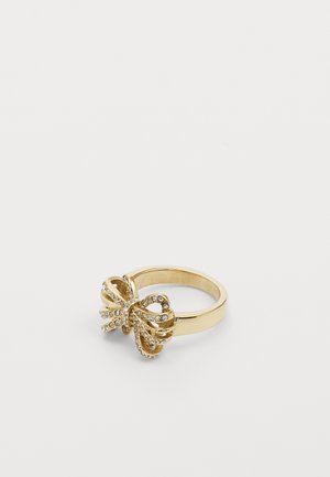 Bague en or avec un design en forme de nœud ornée de petits strass transparents sur fond blanc.