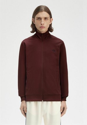 Giacca bordeaux con zip, colletto alto, tasche frontali e un logo discreto. Tessuto liscio e design aderente.