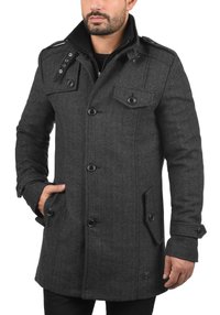 Donkergrijze visgraatjas met een double-breasted ontwerp, brede kraag en knoopdetails. Voorzien van twee zakken aan de voorkant en een gestructureerde stof.