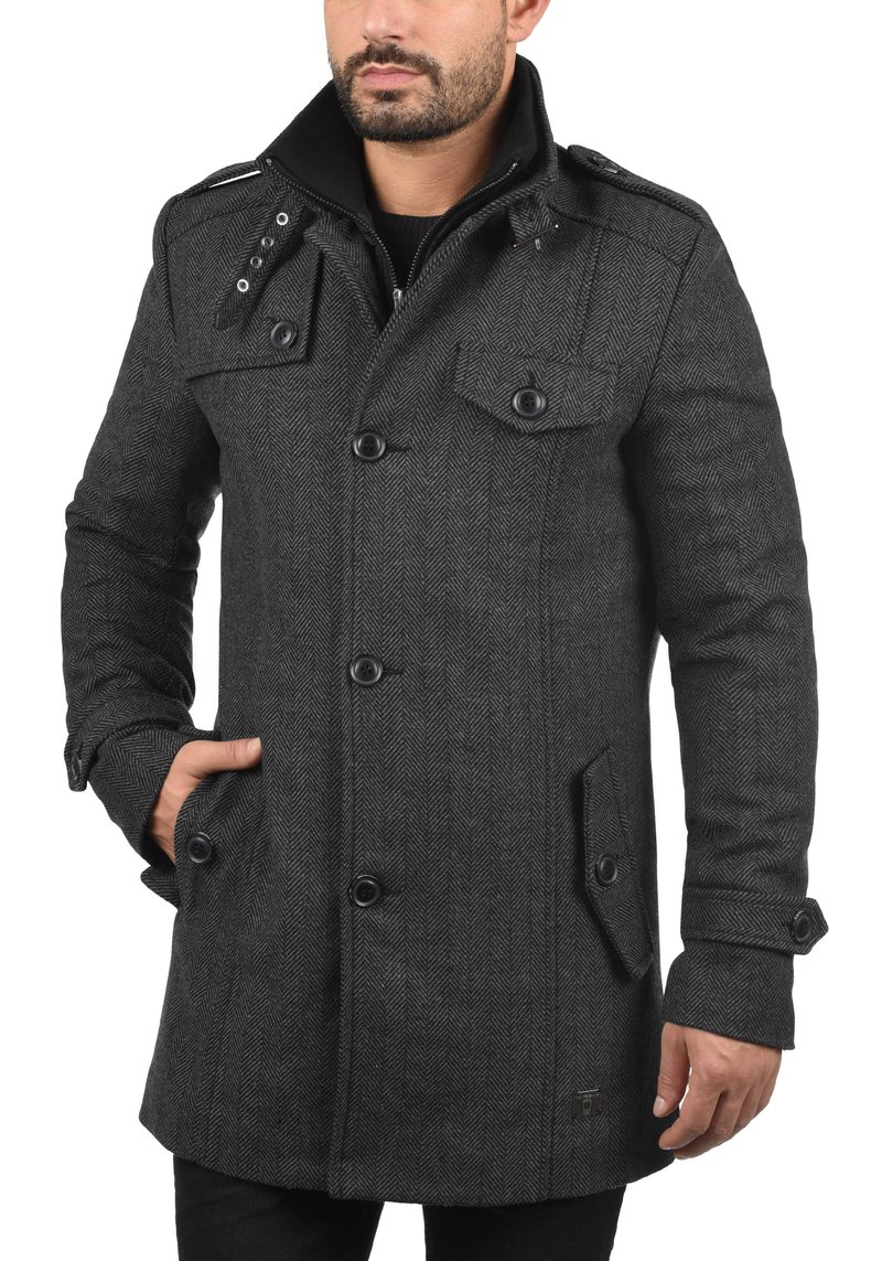 Donkergrijze visgraatjas met een double-breasted ontwerp, brede kraag en knoopdetails. Voorzien van twee zakken aan de voorkant en een gestructureerde stof.