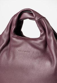 Borsa a tracolla in morbido pelle viola scuro con manico arrotondato e logo "aunts & uncles" impresso al centro anteriore.