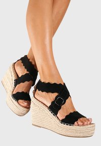 Bottines noires à talons en wedge avec des lanières festonnées, détail de boucle et semelle intermédiaire en jute tressé. Design ouvert au niveau des orteils qui dévoile les ongles. Accents en tissu texturé.