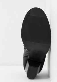 Zapato de cuero negro con una superficie texturizada, tacón cuadrado y suela de goma estriada, mostrando la parte inferior y el perfil del tacón.
