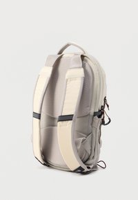 Μπεζ σακίδιο με επενδεδυμένους ιμάντες, λεία ύφανση, πλαϊνές τσέπες με φερμουάρ, ρυθμιζόμενες αγκράφες και λογότυπο στη βάση.