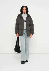 Chaqueta de plumas gris oscuro con capucha, con un cierre frontal de cremallera, mangas ajustadas, combinada con unos jeans azul claro y un bolso tote negro.