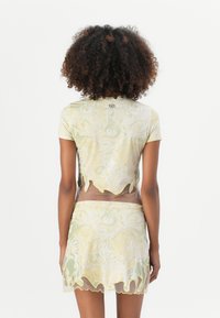 Crop top og miniskjørt sett i gjennomsiktig gul stoff med abstrakte hvite mønstre, med bølgede kanter og en tettsittende design.