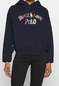Marinblå hoodie i mjukt tyg, med en färgglad "Peace Love Polo"-grafik och en hästlogotyp. Avslappnad passform och dragsko i huven.