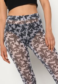 Leggings transparentes com um padrão de borboleta preta sobre um fundo claro, com uma textura suave e um design ajustado.