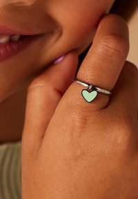 Zilveren ring met een mintgroene harthanger. De ring heeft een gladde band en een kleine hangende charme, die een minimalistisch ontwerp toont.