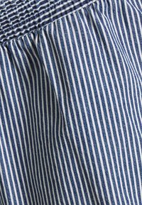Cotton fabric with blue and white vertical stripes, featuring gathered texture along the top edge, creating a ruffled effect.