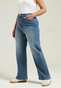 Vaaleansiniset farkut, joissa on lievää haalistumista ja levenevät lahkeet. Niissä on hopeiset niittikoristeet sauman varrella sekä klassinen viiden taskun muotoilu.