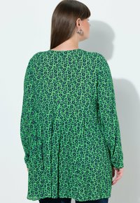 Tunika verde con motivo floreale blu scuro. Tessuto leggero, maniche lunghe, dettaglio arricciato sul retro, scollatura rotonda.