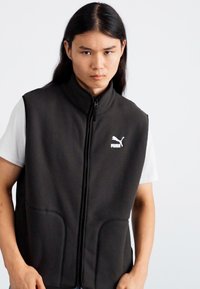 Schwarze ärmellose Weste aus Fleece-Material, mit hohem Kragen, Frontreißverschluss und zwei Seitentaschen. Puma-Logo auf der Brust.