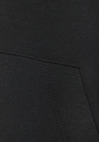 Schwarzer Stoff mit glatter Textur und dezentem Stretch. Er verfügt über eine sichtbare Naht und eine Tasche in der unteren linken Ecke.