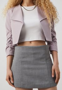 Chaqueta corta de color púrpura claro con mangas fruncidas, combinada con un top corto de canalé blanco y una falda mini ajustada gris con una textura sutil.
