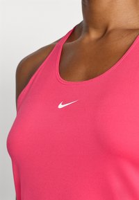 Ružičasta Nike majica bez rukava s glatkom teksturom, sa bijelim logotipom u središtu. Dizajn uključuje okrugli izrez i tanke naramenice.