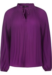 Violetti pitkähihaine paita, joka on valmistettu kevyestä kankaasta. Siinä on pystypleikityksiä, avainaukko kaula-aukossa, joka voidaan sitoa, sekä elastiset hihansuut.