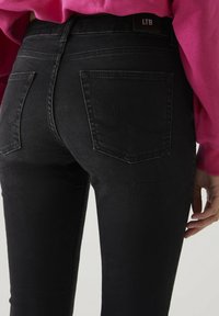 Zwarte denim jeans met een nauwsluitend ontwerp, voorzien van achterzakken en subtiele stiksels, gecombineerd met een roze trui.