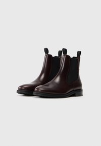 Brune læder Chelsea boots med elastiske sidepaneler, glat finish, sorte såler og hæklede stropper for nem påtagning.