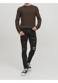Jersey marrón de canalé, vaqueros ajustados negros desgastados y zapatillas negras con suelas blancas. Conjunto casual con textura de tela visible y desgastes.