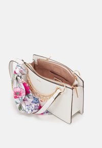 Borsa bianca con sciarpa a stampa floreale attaccata, dettagli in catena dorata, forma strutturata, scomparto con zip e una texture in pelle liscia.