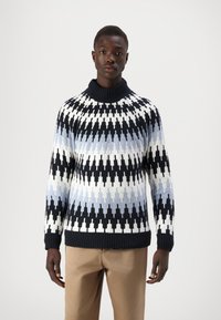 Maglione lavorato a maglia blu navy, bianco e azzurro chiaro con un alto colletto e polsini a coste, caratterizzato da un design geometrico a zigzag.