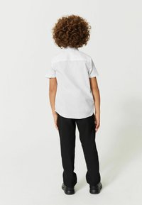 Chemise blanche à manches courtes avec un ourlet arrondi, associée à un pantalon noir et des chaussures noires. Présente une texture lisse et une construction simple.