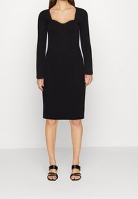 Robe moulante noire côtelée à manches longues avec décolleté carré ; présente des détails texturés sur les côtés et une silhouette ajustée.