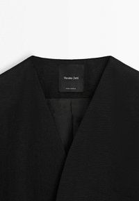 Černý oděv s výstřihem do V, se všitou štítkem "Massimo Dutti" a "Vyrobeno v Maroku" na vnitřní straně límce.