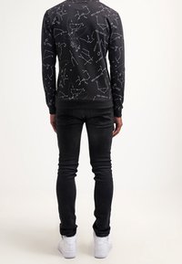 Black sweatshirt with white constellations and equations print; fitted, round neck, long sleeves. Paired with slim-fit black jeans and white sneakers.