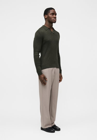 Maglione verde scuro a coste con collo polo, abbinato a pantaloni beige chiaro a gamba larga e scarpe nere. Tessuto liscio, design aderente.