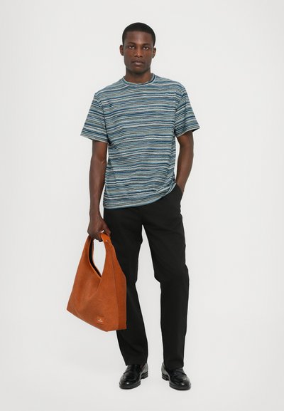 T-shirt à rayures à manches courtes en bleu et blanc, associé à un pantalon noir et tenant un sac texturé marron. Des chaussures noires complètent le look.
