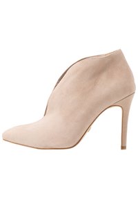 Beige semišové kotníkové boty s špičatou špičkou, otevřeným bočním designem a vysokým jehlovým podpatkem. Hladký povrch s minimálním viditelným prošíváním.