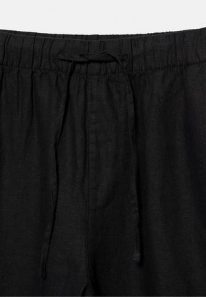 Pantaloni con vita elastica nera e coulisse in tessuto legata a fiocco al centro davanti.