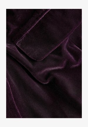Tissu en velours violet avec une texture lisse et un léger éclat, comportant des sections pliées et un bord net. Aucun matériel ou motif visible.