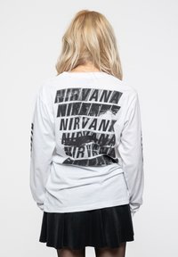 White long-sleeve t-shirt featuring repeated black text of "Nirvana" in varying sizes and orientations on the back. Cotton fabric, relaxed fit.