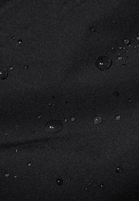 Wasserabweisender schwarzer Stoff mit einer glatten Textur, der mehrere kleine Wassertropfen auf der Oberfläche zeigt und seine feuchtigkeitsbeständigen Eigenschaften hervorhebt.