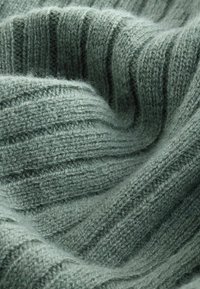 Tissu côtelé texturé dans une douce teinte verte, mettant en valeur des fils fins et des variations subtiles de teinte, créant une apparence chaleureuse et accueillante.
