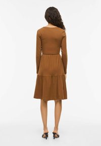 Robe longue marron à manches longues avec un corsage ajusté et une jupe à volants. Fabriquée en tissu doux, elle présente un col rond et un détail de coutures minimalistes.