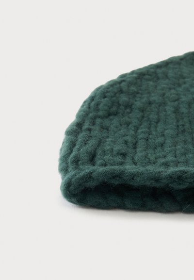 Gros plan d'un bonnet en laine tricotée vert foncé avec bord replié côtelé sur fond blanc.