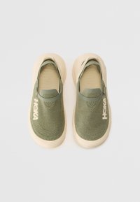 Slip-on shoes in olive green fabric with textured surface and beige rubber soles. Features logo on the side and a seamless upper design.