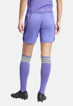 Paarse sportshorts en kousen tot de knie met groene en blauwe strepen, gecombineerd met zwarte voetbalschoenen. Soepel, lichtgewicht materiaal.