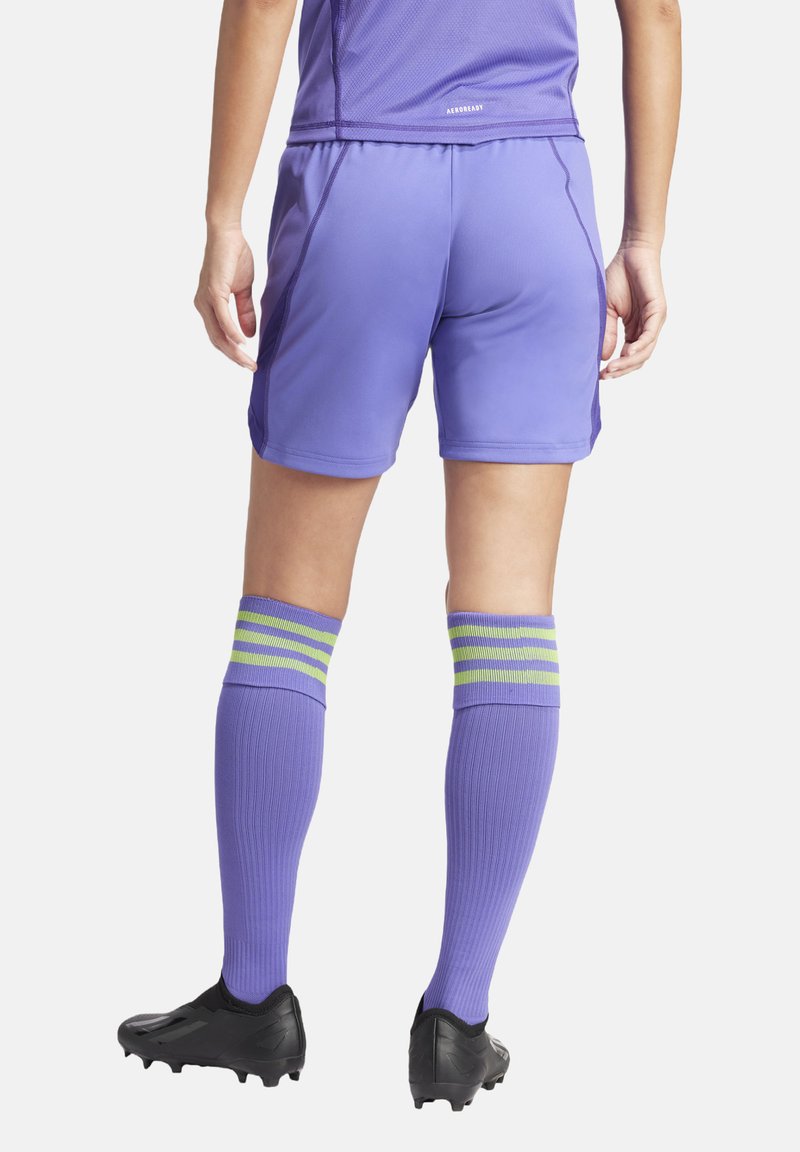 Paarse sportshorts en kousen tot de knie met groene en blauwe strepen, gecombineerd met zwarte voetbalschoenen. Soepel, lichtgewicht materiaal.