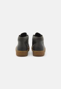 Botas de tobillo de cuero negro con una suela de corcho marrón texturizada. El diseño presenta un corte superior suave y un collar acolchado para mayor comodidad.