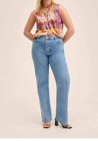 Top sin mangas con estampado en tonos rosa, amarillo y naranja; jeans de tiro alto de color azul con pierna recta y detalle de dobladillo sin rematar. Sandalias de tacón negras.